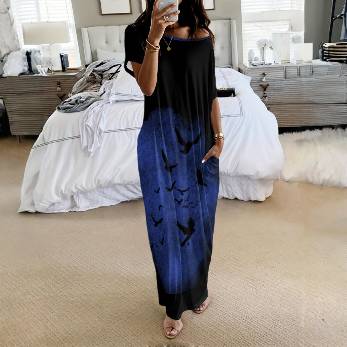 Woman wearing a black and blue dress with bird patterns in a bedroom.