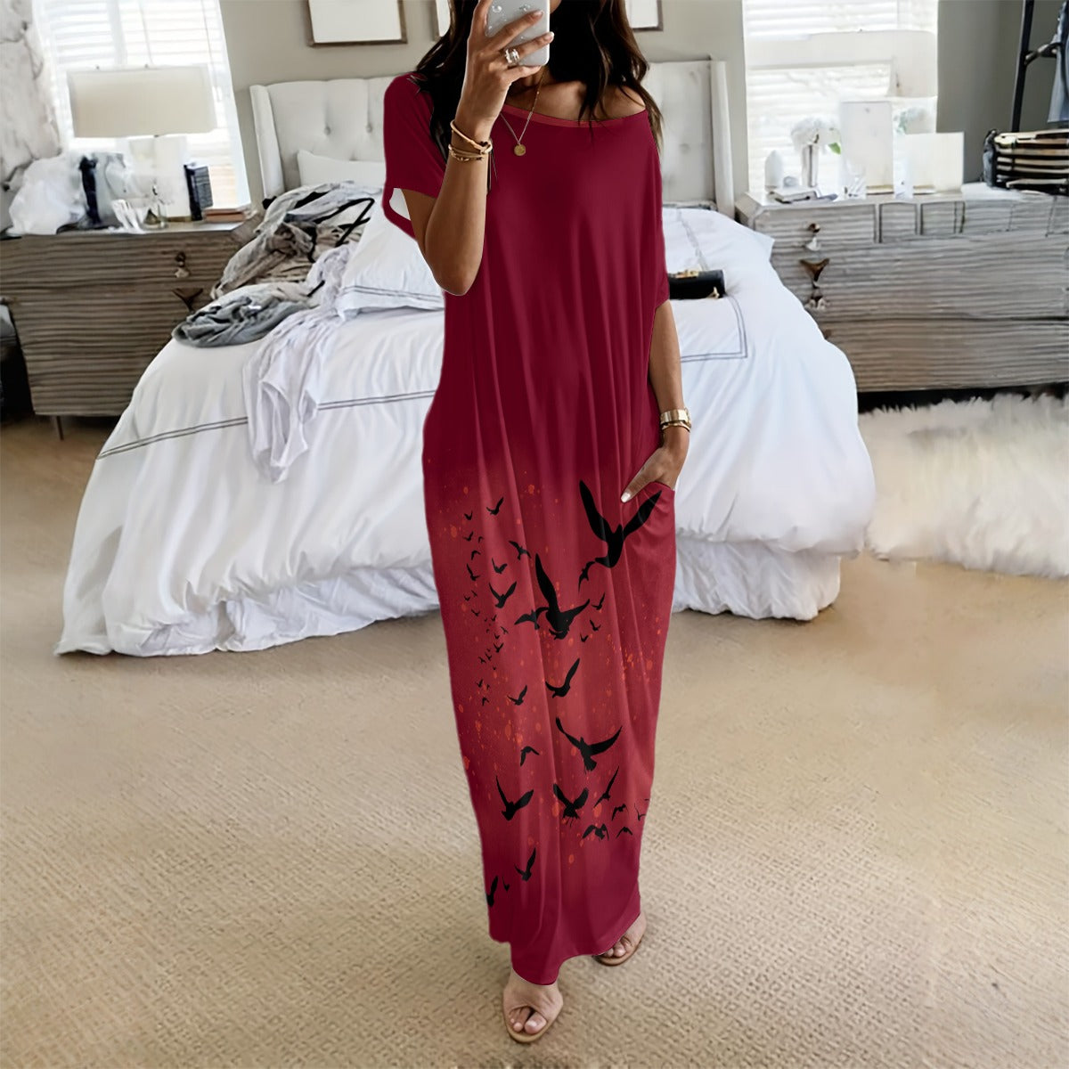 Woman taking a mirror selfie wearing a red dress with black bird patterns in a bedroom.