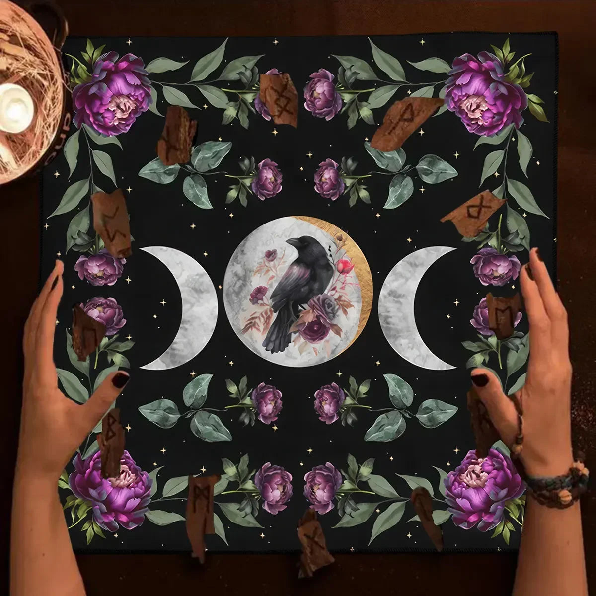 Hands holding a black box with floral and moon designs, including a crow and purple flowers.