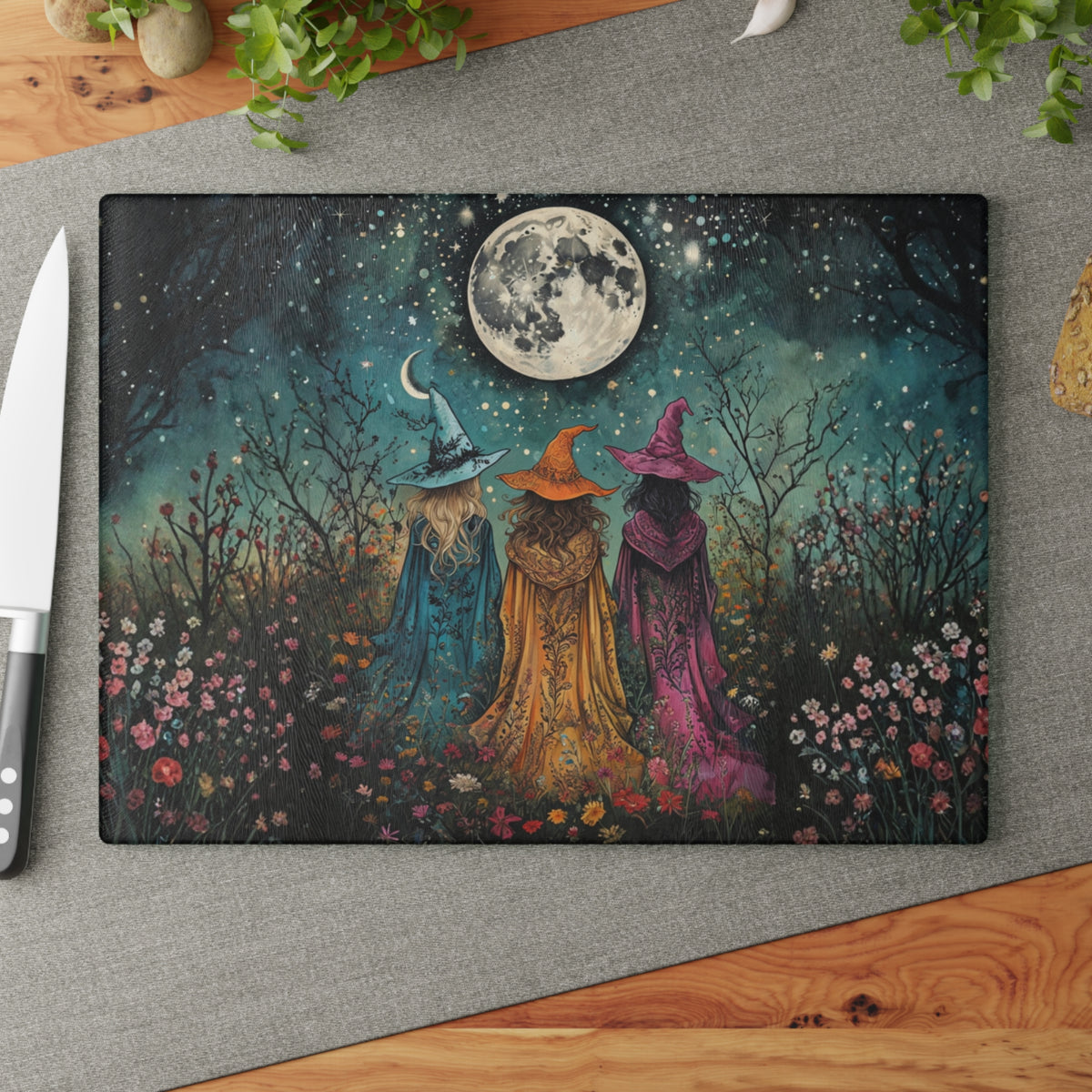 Decorative cutting board with three witches in colorful hats against a night sky with a moon, on a gray surface.