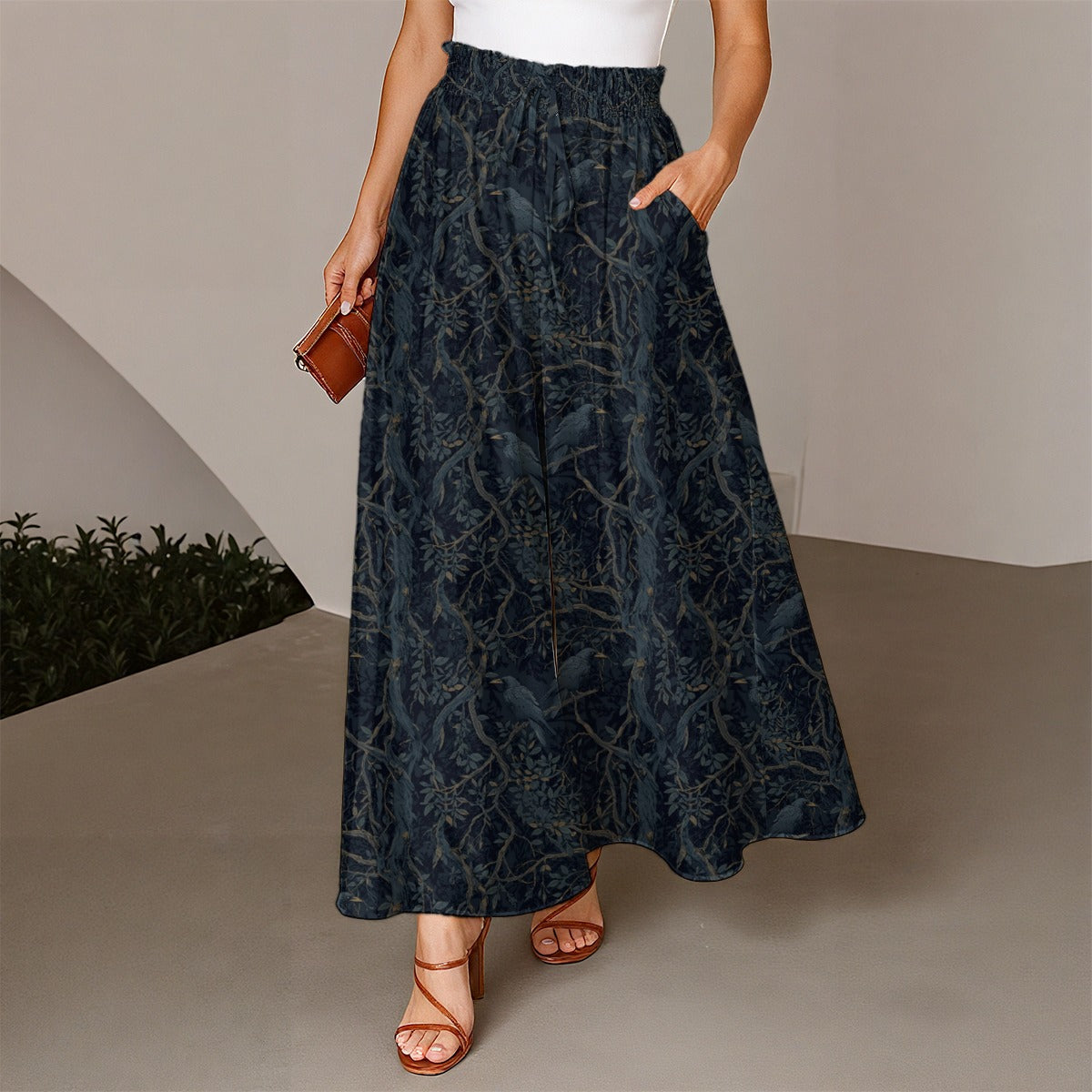Person wearing a dark blue floral patterned skirt with a white top and brown sandals, holding a small brown bag.